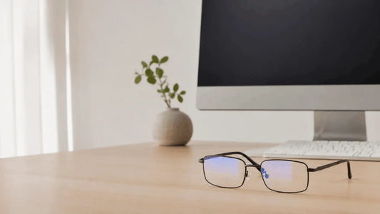 Ochelari cu protecție lumină albastră așezați lângă un monitor de birou